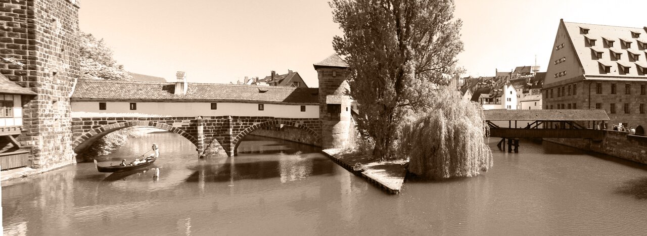Sepiaaufnahme von einer bebauten Steinbrücke und einem Holzsteg über die Pegnitz, dazwischen eine kleine Insel mit Bäumen, im Wasser eine venezianische Gondel